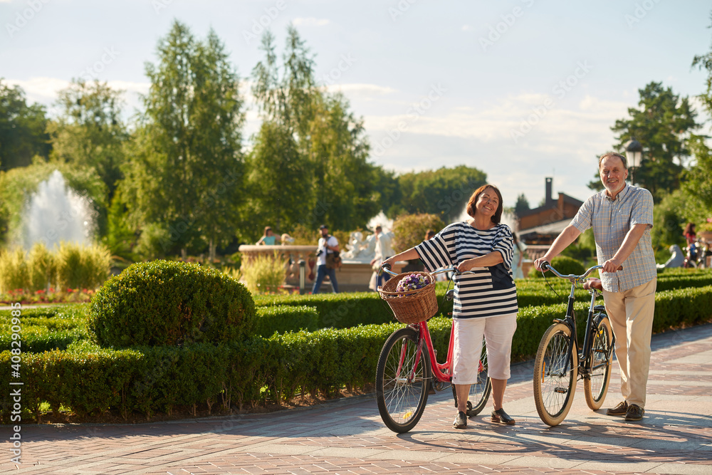 Fototapeta premium Senior man and woman with bikes outdoors. Sunny city park background.
