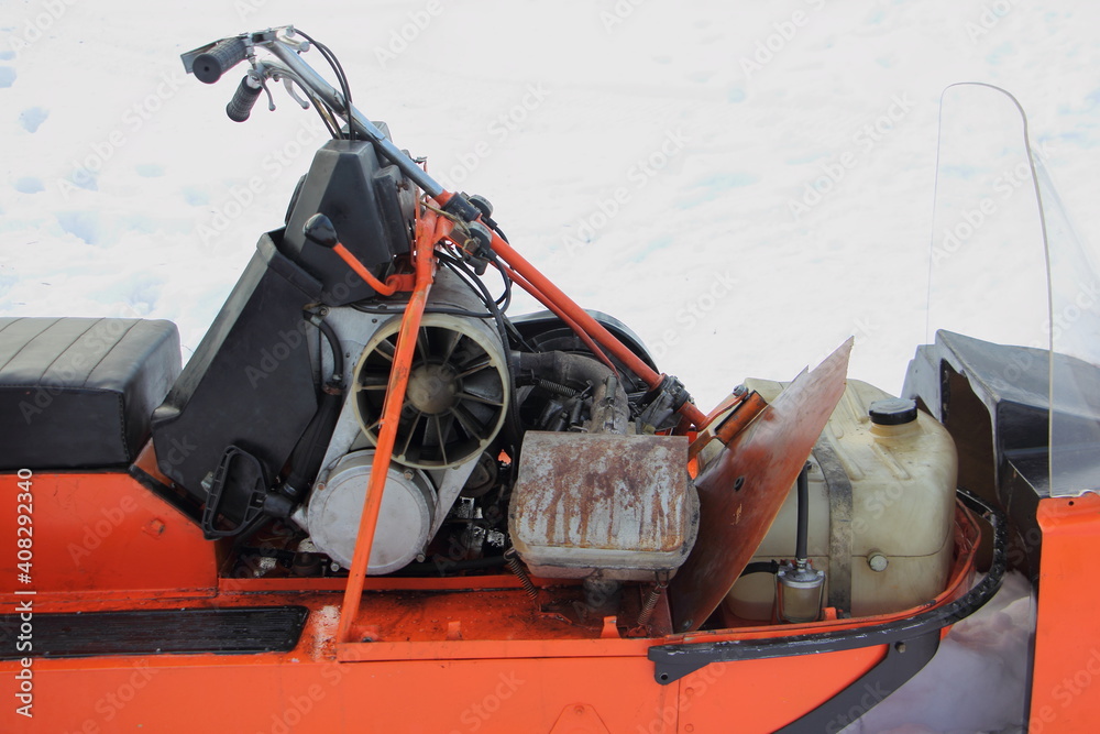 Old vintage Russian utility snowmobile without cover closeup - steering, air cooled engine with emergency motor start handle and fuel tank
