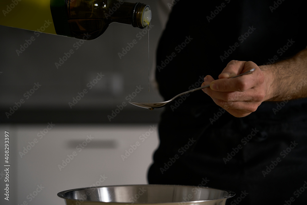A man's hands add olive oil from the bottle into the wholemeal flour dough to make homemade bread, pasta, cake or pizza.