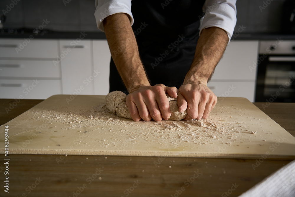 The hands of the strong man knead the dough from which they will make bread, pasta, cake or pizza. In his kitchen he carries on the tradition of homemade pasta. A cloud of white flour flies like dust. The hands of the strong man knead the dough from which they will make bread, pasta, cake or pizza. In his kitchen he carries on the tradition of homemade pasta. A cloud of white flour flies like dust.
