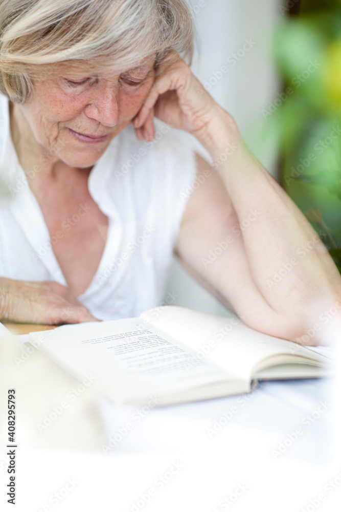 Seniorin sitzt hinter einem Fenster und liest