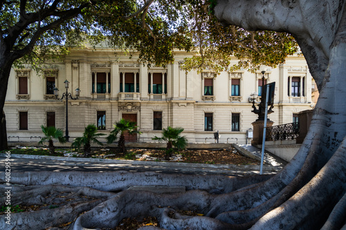 Old trees framing a liberty style building on Reggio Calabria's waterfront promenade, Italy.