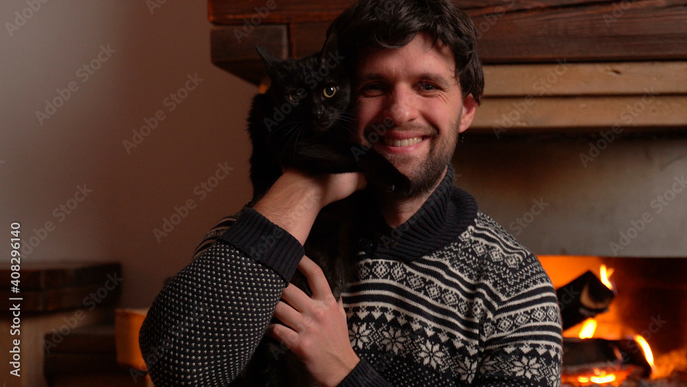 Young man holds a cat in his arms while sitting by the fireplace. Young man holds a cat in his arms while sitting by the fireplace.