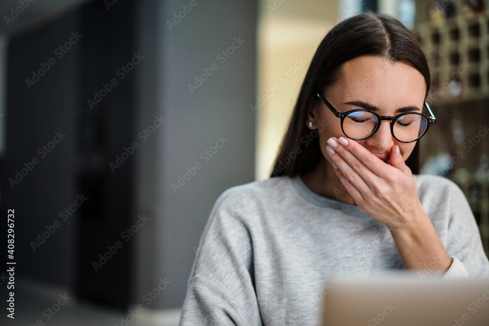 Tired young woman in eyeglasses yawning while working with laptop Tired young woman in eyeglasses yawning while working with laptop