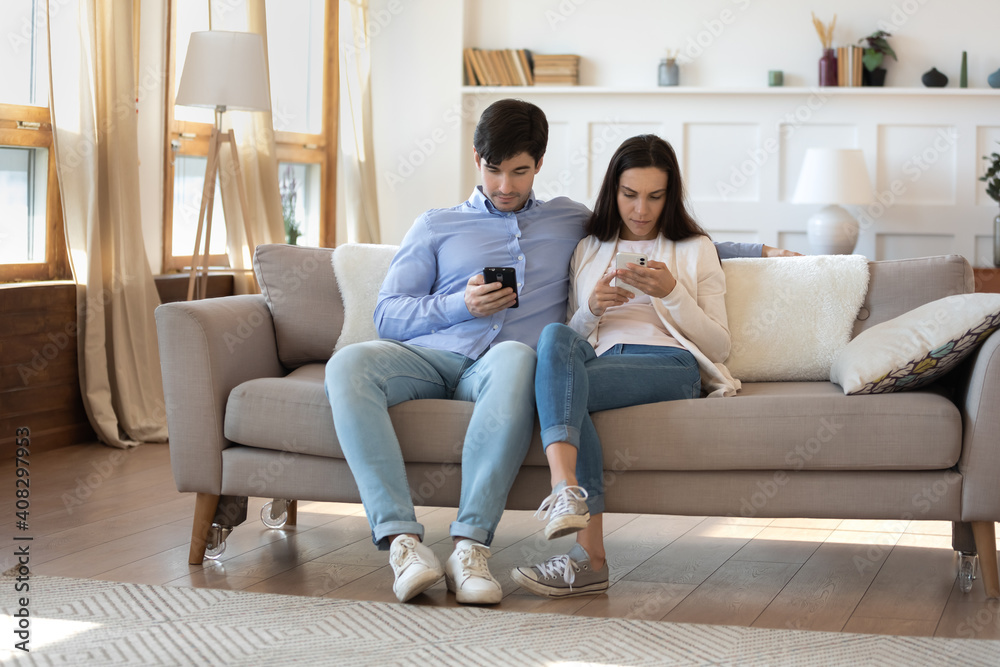 Obsessed man and woman using phones, ignoring each other, sitting on couch together, young couple looking at smartphones screen, chatting on social network, not talking, gadget addiction concept
