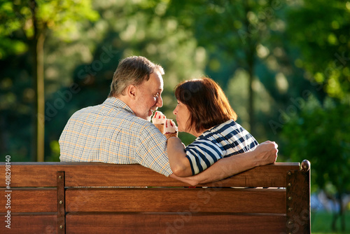 Man and woman enjoying cone ice-cream outdoors. Back view retired couple eating ice-cream on the park bench.