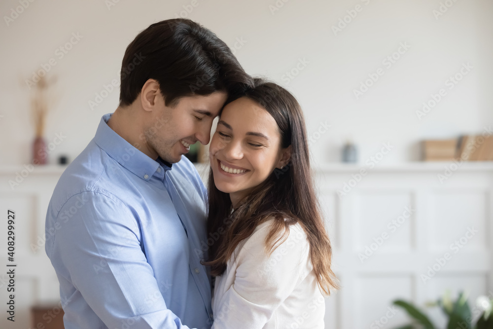 Close up happy young couple hugging, smiling woman and man enjoying tender moment, standing at home, happy attractive wife and husband touching foreheads, expressing love and care, romantic date Close up happy young couple hugging, smiling woman and man enjoying tender moment, standing at home, happy attractive wife and husband touching foreheads, expressing love and care, romantic date