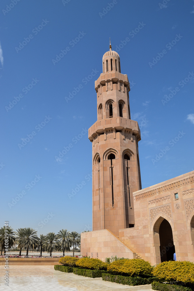 A minaret in contrast with the blue sky in Sultan Qaboos Grand Mosque. In the background, there are palm trees. Muscat, Oman.