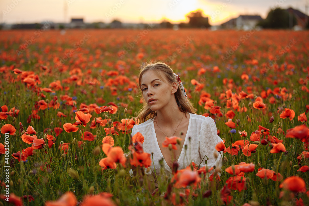 Naklejka premium portrait of a girl in a white dress in a field of red poppies