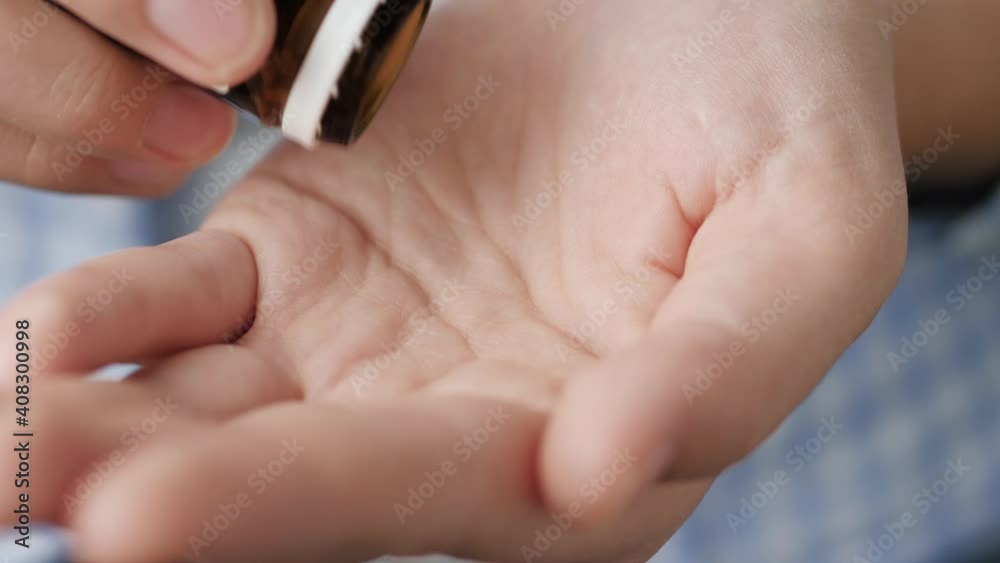Two small orange round pills fall into palm of hand from pill bottle. Close-up, front view, center composition Two small orange round pills fall into palm of hand from pill bottle. Close-up, front view, center composition