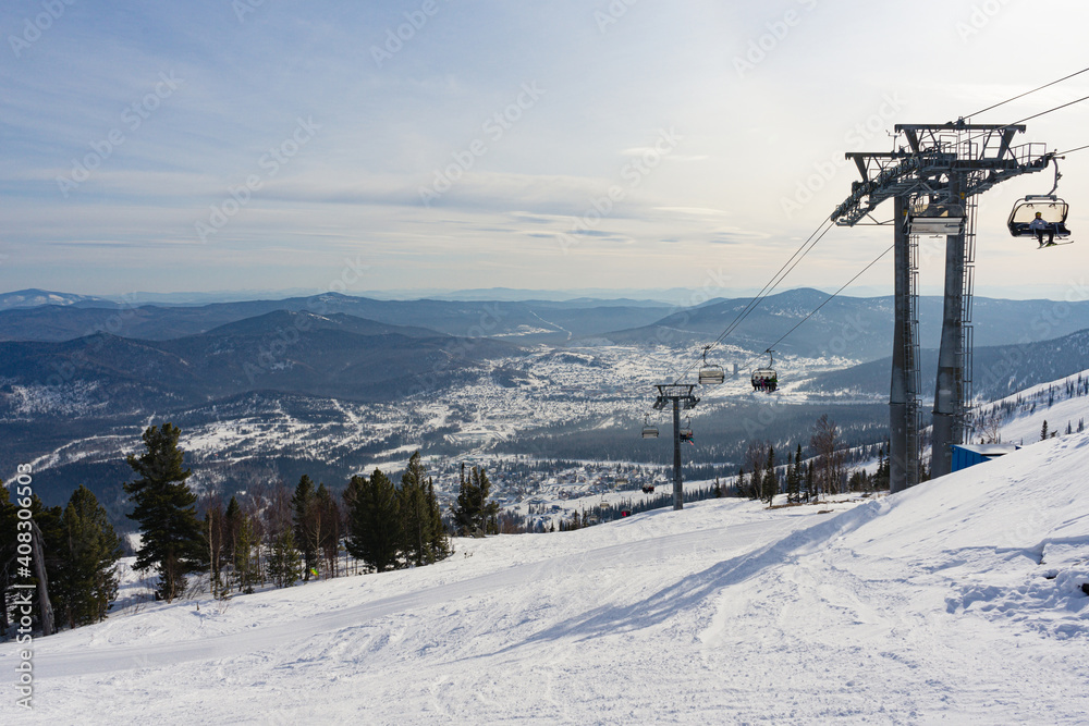 Sheregesh Winter ski resort in Russia. Skiers and snowboarders move on a lockable chair ski lift. Mountains, view of the village. Sheregesh Winter ski resort in Russia. Skiers and snowboarders move on a lockable chair ski lift. Mountains, view of the village.