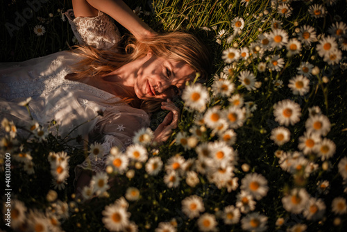 Playful portrait of natural young woman relaxing laying in grass full of daisies. Smiling gal looking into camera