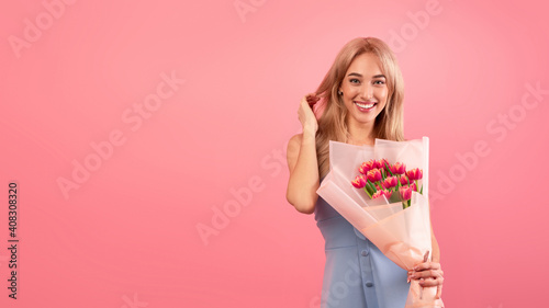 Millennial lady in romantic dress holding bunch of tulpis over pink background, banner design with free space