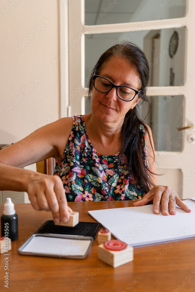 Middle-aged woman putting a decorative stamp on a sheet of paper. Vertical shot. Middle-aged woman putting a decorative stamp on a sheet of paper. Vertical shot.