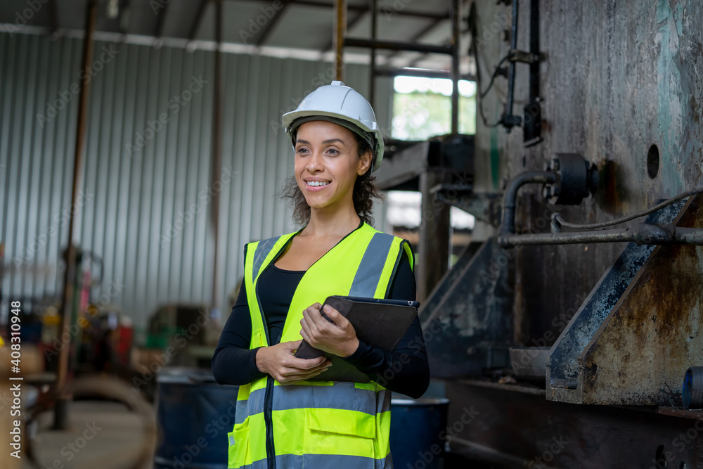 Young female in protective uniform inspecting industrial machine and taking necessary notes on digital tablet at plant. Young female in protective uniform inspecting industrial machine and taking necessary notes on digital tablet at plant.