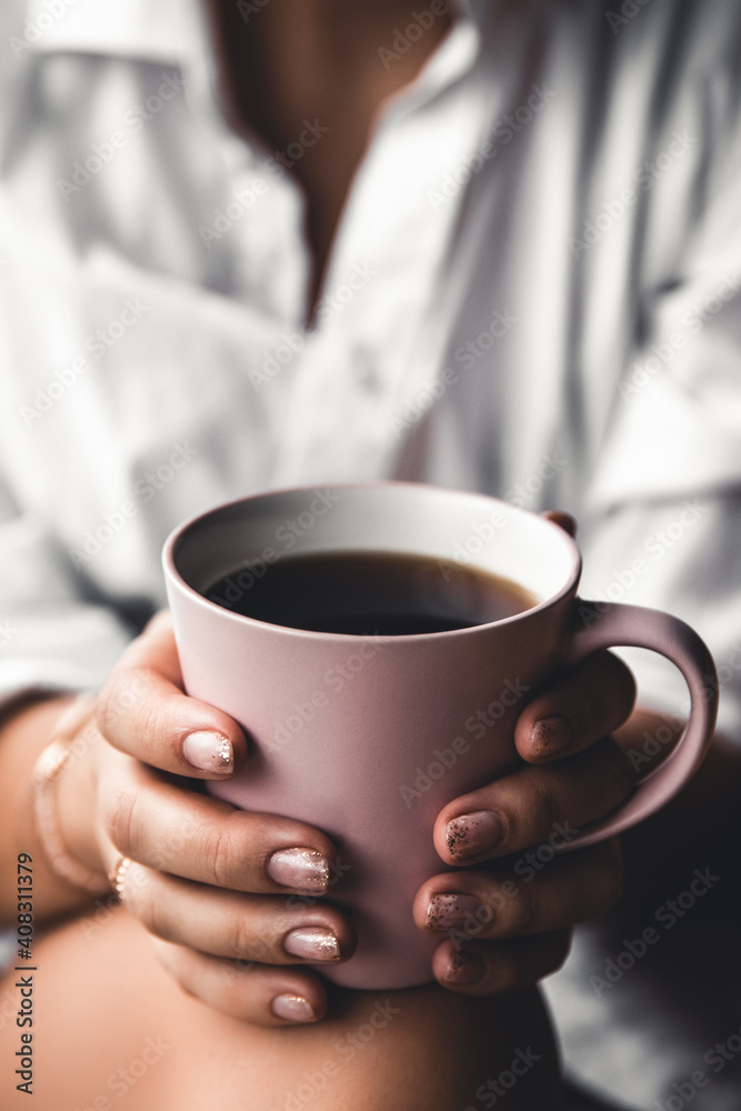Woman in a white t-shirt holds morning coffee in a pink ceramic cup. Manicure. Front view Woman in a white t-shirt holds morning coffee in a pink ceramic cup. Manicure. Front view