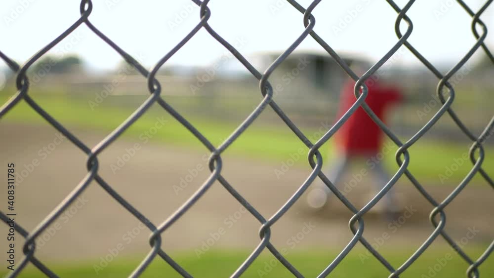 Little league player swinging during practice, defocused behind fence Little league player swinging during practice, defocused behind fence