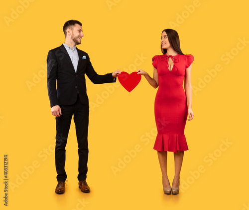 Loving Couple Holding Red Heart Standing Over Yellow Studio Background