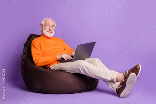 Full size profile photo of aged man sitting big soft chair use laptop isolated on violet color background