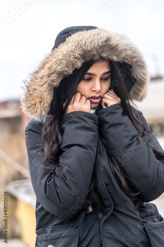 Cute young woman freezing in winter coat standing in street
