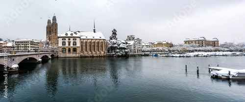 Panoramic view of Grossm  nster church in snow covered Zurich city Switzerland from across the Limmat river winter time cloudy day