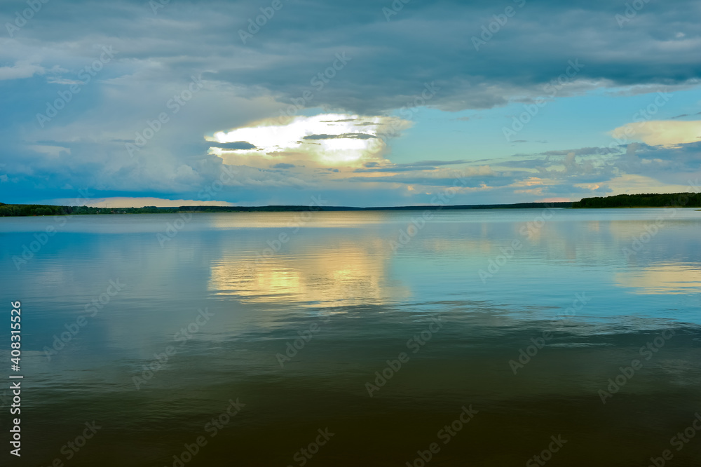 A calm evening sky landscape of pastel colors with a reflection in the smooth waves of a large lake. Natural background
