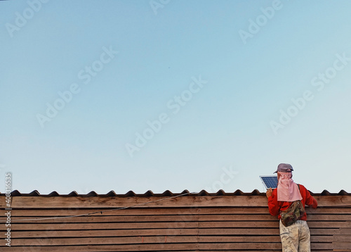 Asian man is setting a solar cell or Photovoltaics module (PV module, Solar module) on the roof with blue sky.