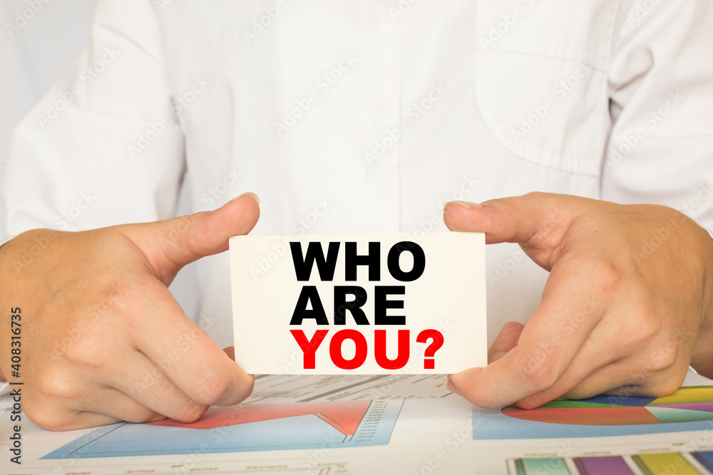 a man in the office holds a card with text WHO ARE YOU . business concept a man in the office holds a card with text WHO ARE YOU . business concept