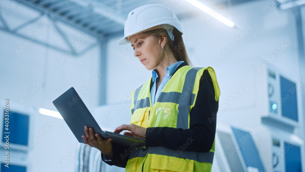 High-Tech Factory: Confident and Professional Female Engineer Wearing Safety Jacket and Hard Hat Holding and Working on Laptop Computer. Modern Bright Industrial Facility. Low Angle Shot High-Tech Factory: Confident and Professional Female Engineer Wearing Safety Jacket and Hard Hat Holding and Working on Laptop Computer. Modern Bright Industrial Facility. Low Angle Shot