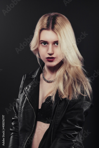 A beautiful, glamour young blond Girl dressed in a black jacket is posing on black background