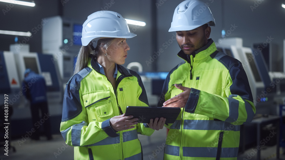 Chief Engineer and Project Manager Wearing Safety Vests and Hard Hats, Use Digital Tablet Computer in Modern Factory, Talking, Optimizing Production Line. Industrial Facility with CNC Machinery Chief Engineer and Project Manager Wearing Safety Vests and Hard Hats, Use Digital Tablet Computer in Modern Factory, Talking, Optimizing Production Line. Industrial Facility with CNC Machinery