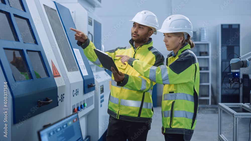 Chief Engineer and Project Manager Wearing Safety Vests and Hard Hats, Use Digital Tablet Controller in Modern Factory, Talking, Optimizing CNC Machinery, Programming Machine for Increasing Efficiency Chief Engineer and Project Manager Wearing Safety Vests and Hard Hats, Use Digital Tablet Controller in Modern Factory, Talking, Optimizing CNC Machinery, Programming Machine for Increasing Efficiency