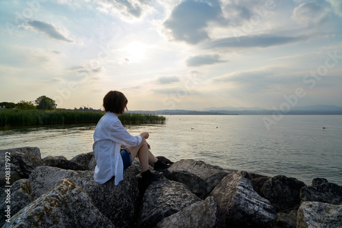 Woman's hands holding a smartphone and make photo during sunset on the lake. Travel photography taken a memory of the garda lake.