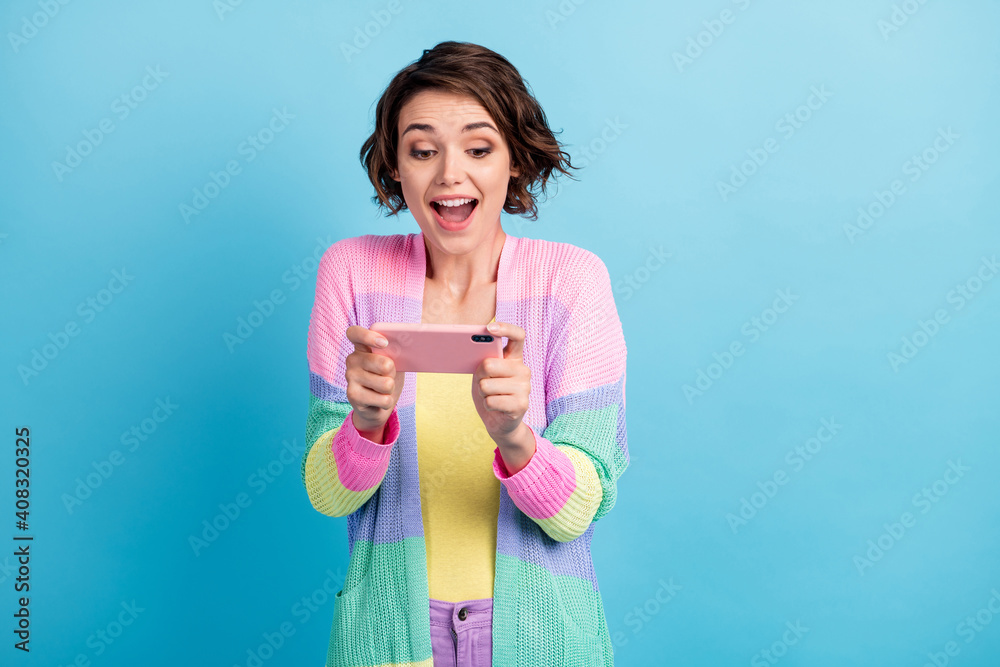 Photo portrait of excited girl playing video games on phone holding in two hands horizontally isolated on pastel blue colored background Photo portrait of excited girl playing video games on phone holding in two hands horizontally isolated on pastel blue colored background