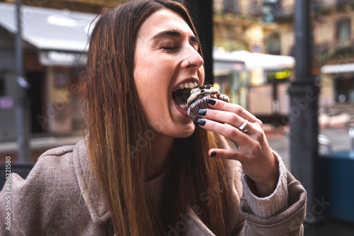 Young caucasian girl enjoying a chocolate cupcake having breakfast at a terrace outdoors.