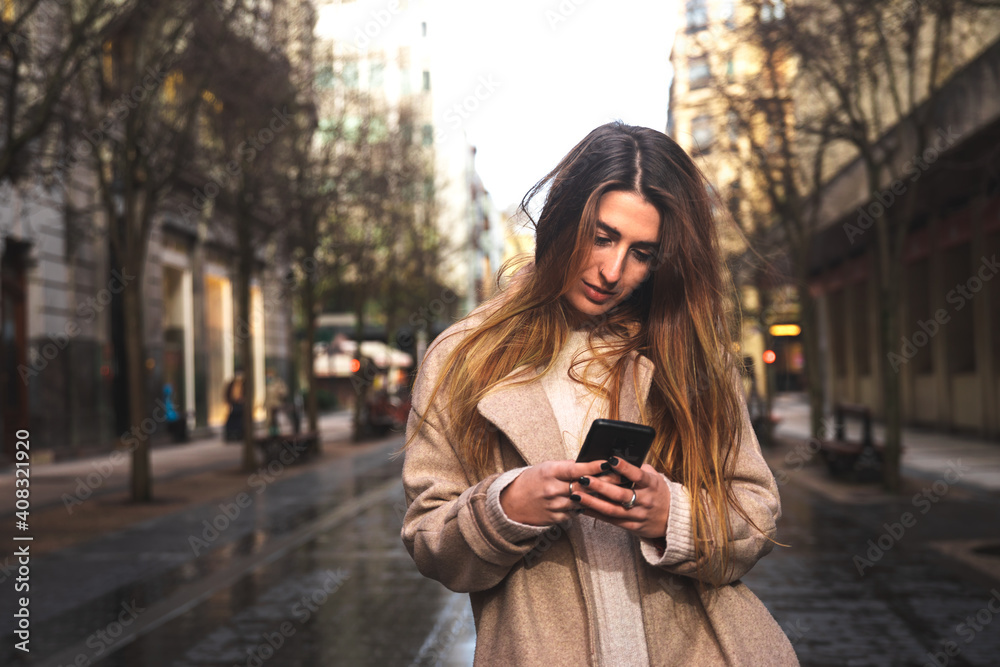 Obraz premium Young caucasian brunette woman using a smartphone at the street