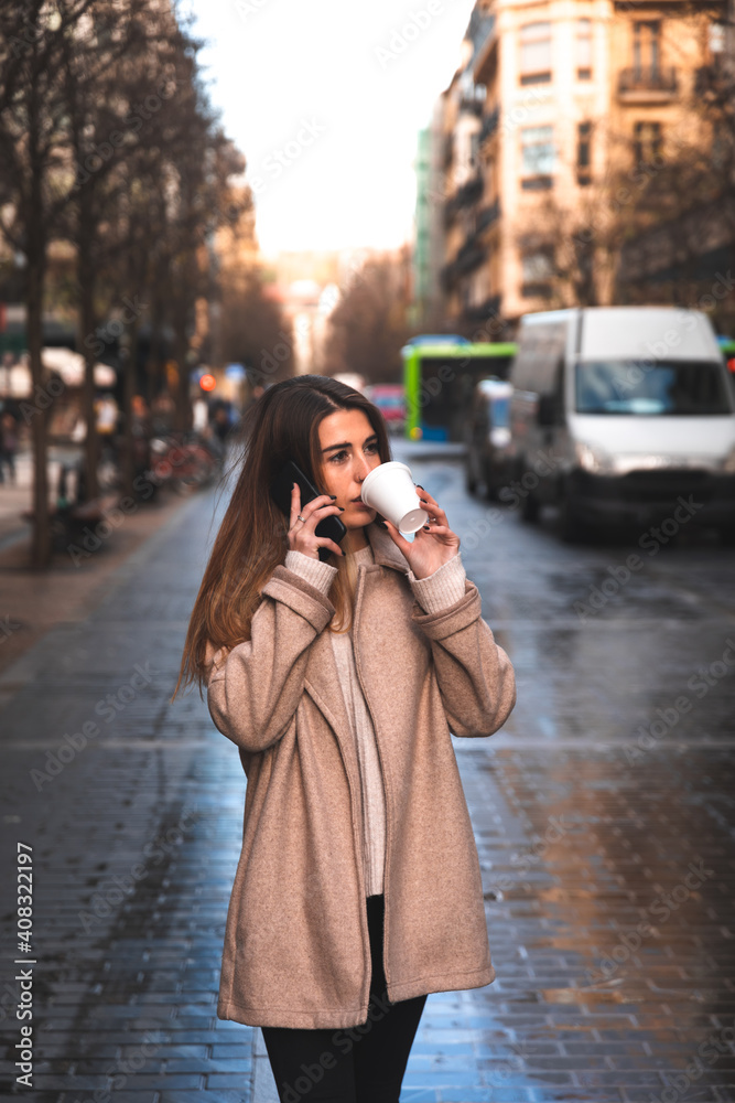 Young caucasian woman talking by phone while drinking a coffee in a plastic cup at Donostia-San Sebastian downtown; Basque Country.