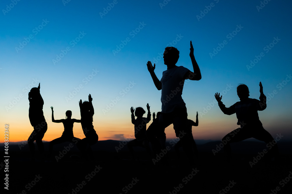 A group of silhouettes of people doing stretching and toning exercises after the running session or during a yoga class somewhere outdoors at sunset. Healthy living in a healthy body. A group of silhouettes of people doing stretching and toning exercises after the running session or during a yoga class somewhere outdoors at sunset. Healthy living in a healthy body.