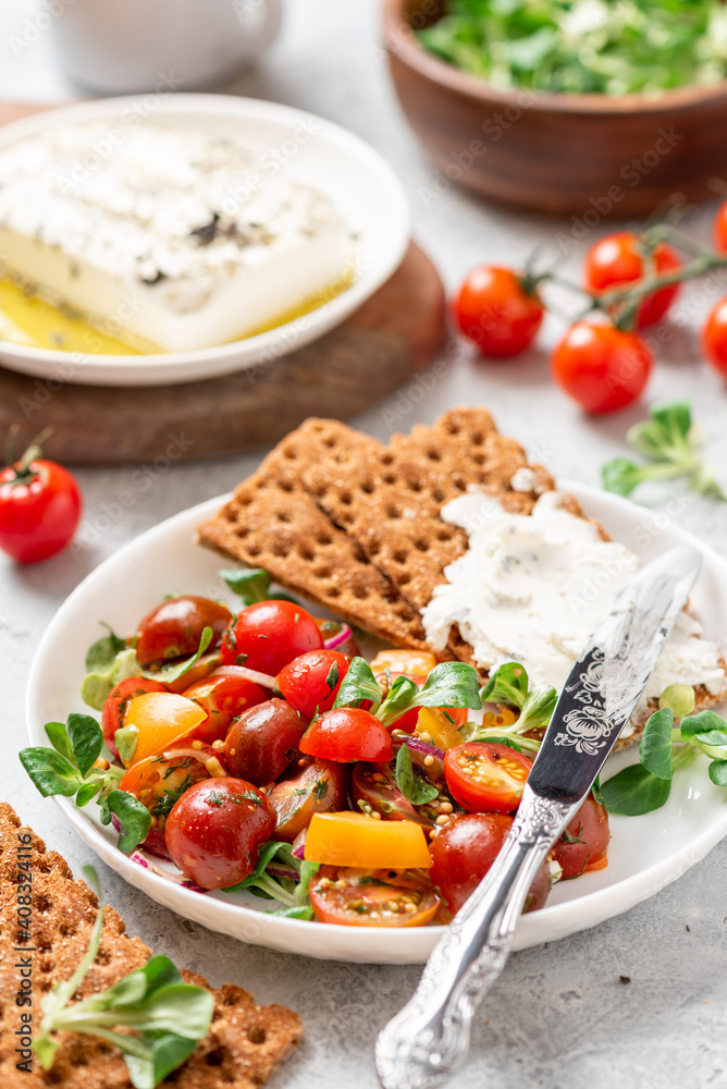 Tasty and healthy breakfast or lunch. Salad of colorful cherry tomatoes, onions, herbs, and olive oil, served with crispbread and feta cheese. Tasty and healthy breakfast or lunch. Salad of colorful cherry tomatoes, onions, herbs, and olive oil, served with crispbread and feta cheese.