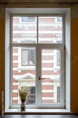 A vase of flowers stands on the window and withered flowers are placed in it