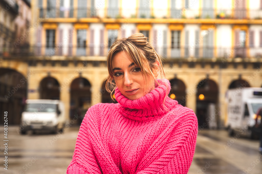 Portrait of a young caucasian blonde woman wearing a pink sweater at the main square from Donostia-San Sebastian; Basque Country.
