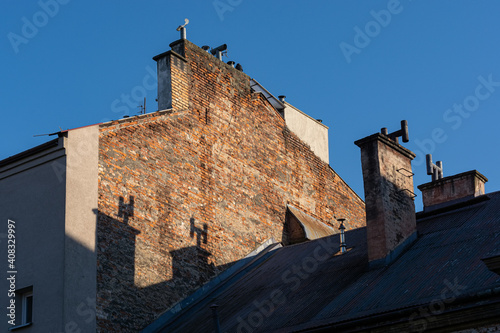 Bilde på lerret Old tenement houses in Cracow lit by the sun against a blue sky - chimneys on th