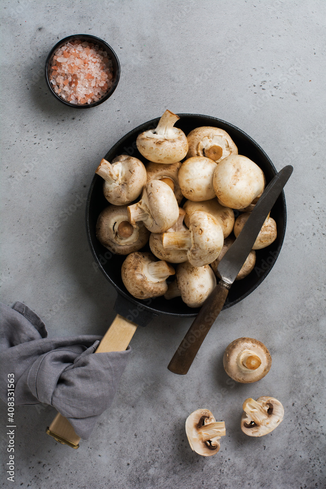 Raw mushrooms champignon in cast-iron old pan on an old concrete gray rustic background for frying. Top view. Raw mushrooms champignon in cast-iron old pan on an old concrete gray rustic background for frying. Top view.