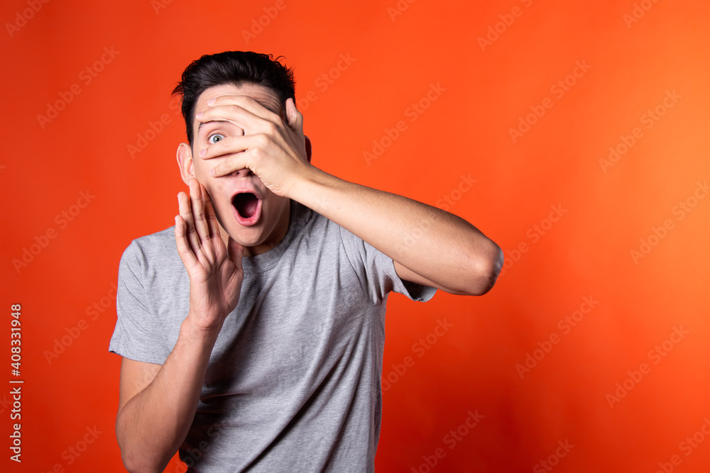 The young guy overhears and is surprised. Orange background. Blue jacket. Emotions and feelings. The young guy overhears and is surprised. Orange background. Blue jacket. Emotions and feelings.