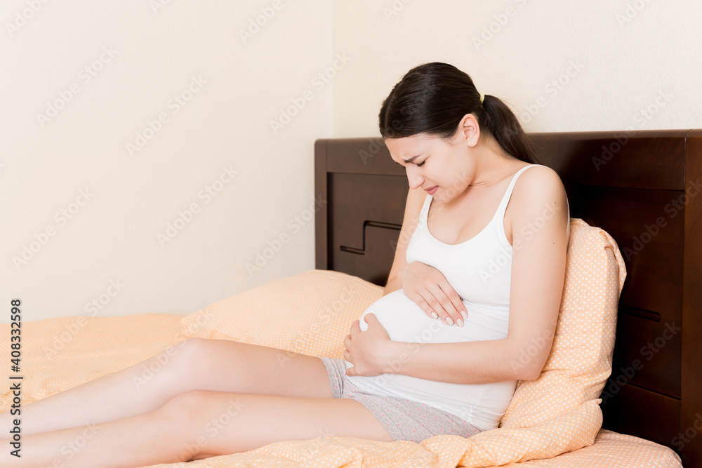 Pregnant Lady Having Massaging Lower belly Sitting On Sofa Indoor. Pregnancy Problems Concept. Maternity healthcare Pregnant Lady Having Massaging Lower belly Sitting On Sofa Indoor. Pregnancy Problems Concept. Maternity healthcare