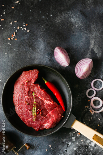 One raw beef steak with spices, onions and chili on dark slate or concrete background. Top view