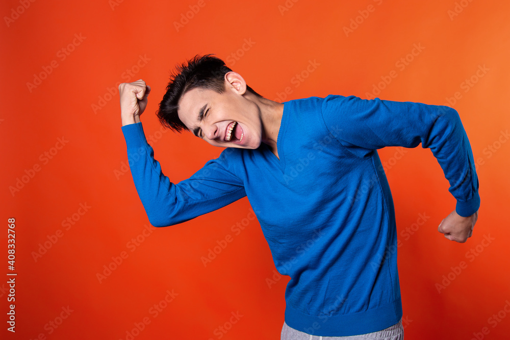 The young guy is happy about the victory. Feelings and emotions. Orange background.