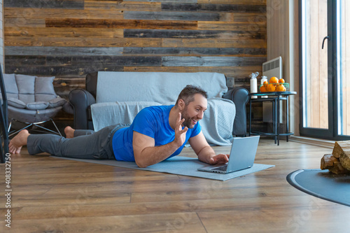 A man during an online video conversation. He lies on the floor while in front of a laptop monitor.