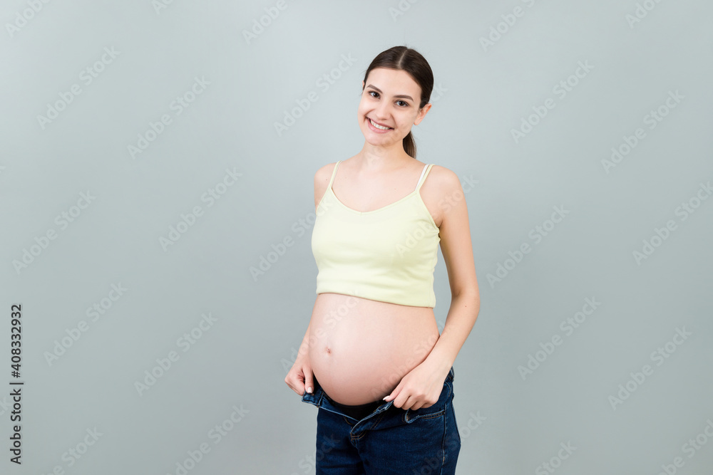 Happy pregnant woman in unzipped jeans showing her naked belly at colorful background with copy space. Baby expecting concept Happy pregnant woman in unzipped jeans showing her naked belly at colorful background with copy space. Baby expecting concept
