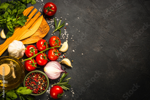 Food cooking background on black stone table. Fresh vegetables, spices, herbs and kitchen utensil. Ingredients for cooking. Top view with copy space.